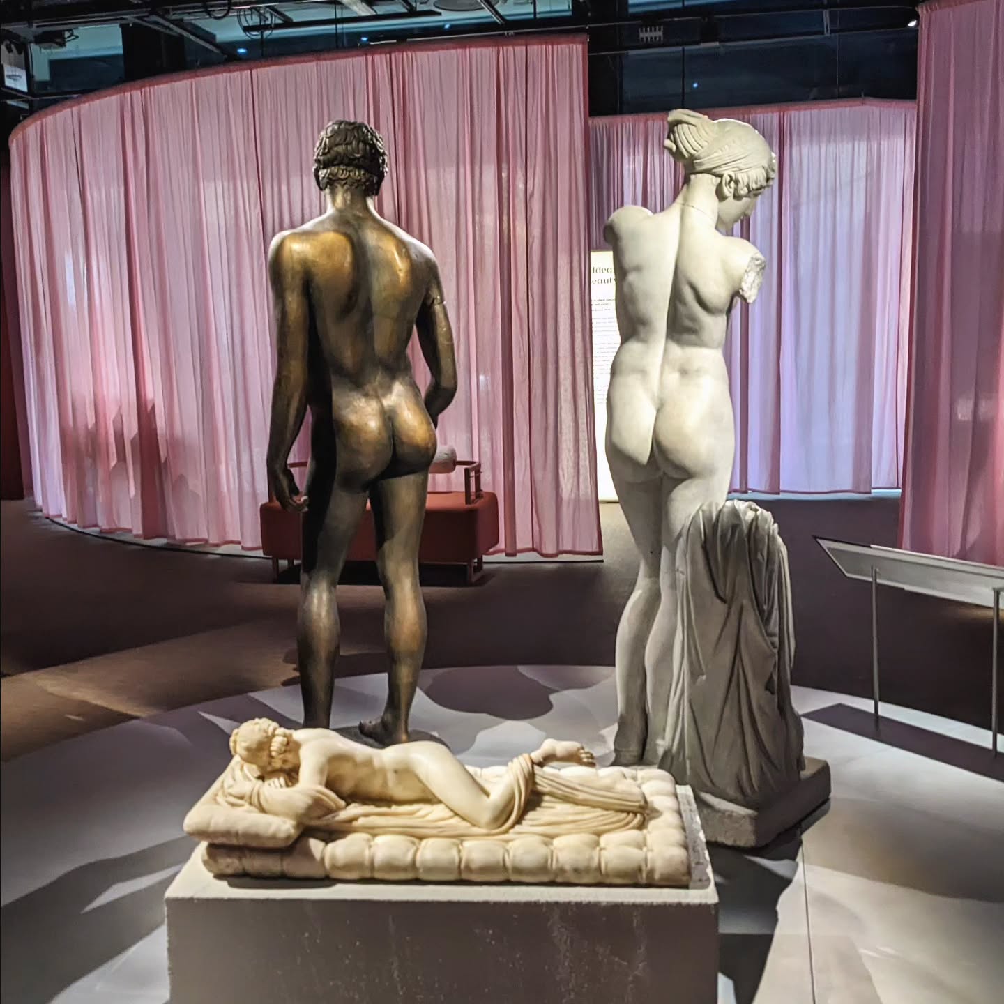 Three classical sculptures made of bronze and marble displayed in front of a pink curtain as part of the Cult of Beauty exhibition at Wellcome Collection.