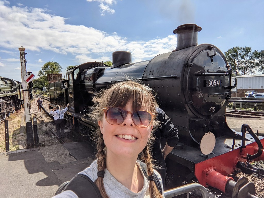 Olivia wearing sunglasses, standing in front of a black steam train.